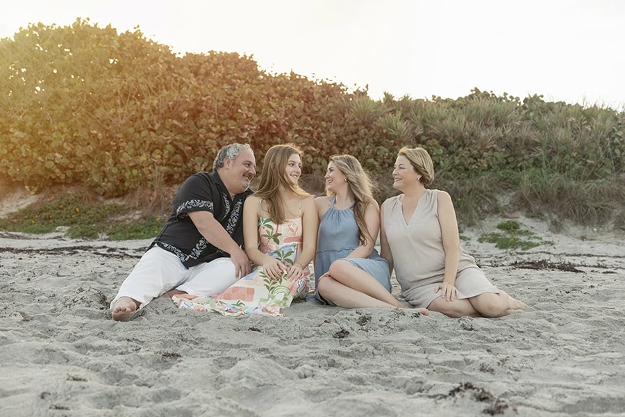 Family sitting in the sand on Melbourne beach looking at each other during sunset.