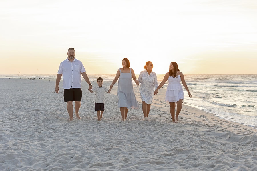 family walking along the beach at sunrise with sun behind them.